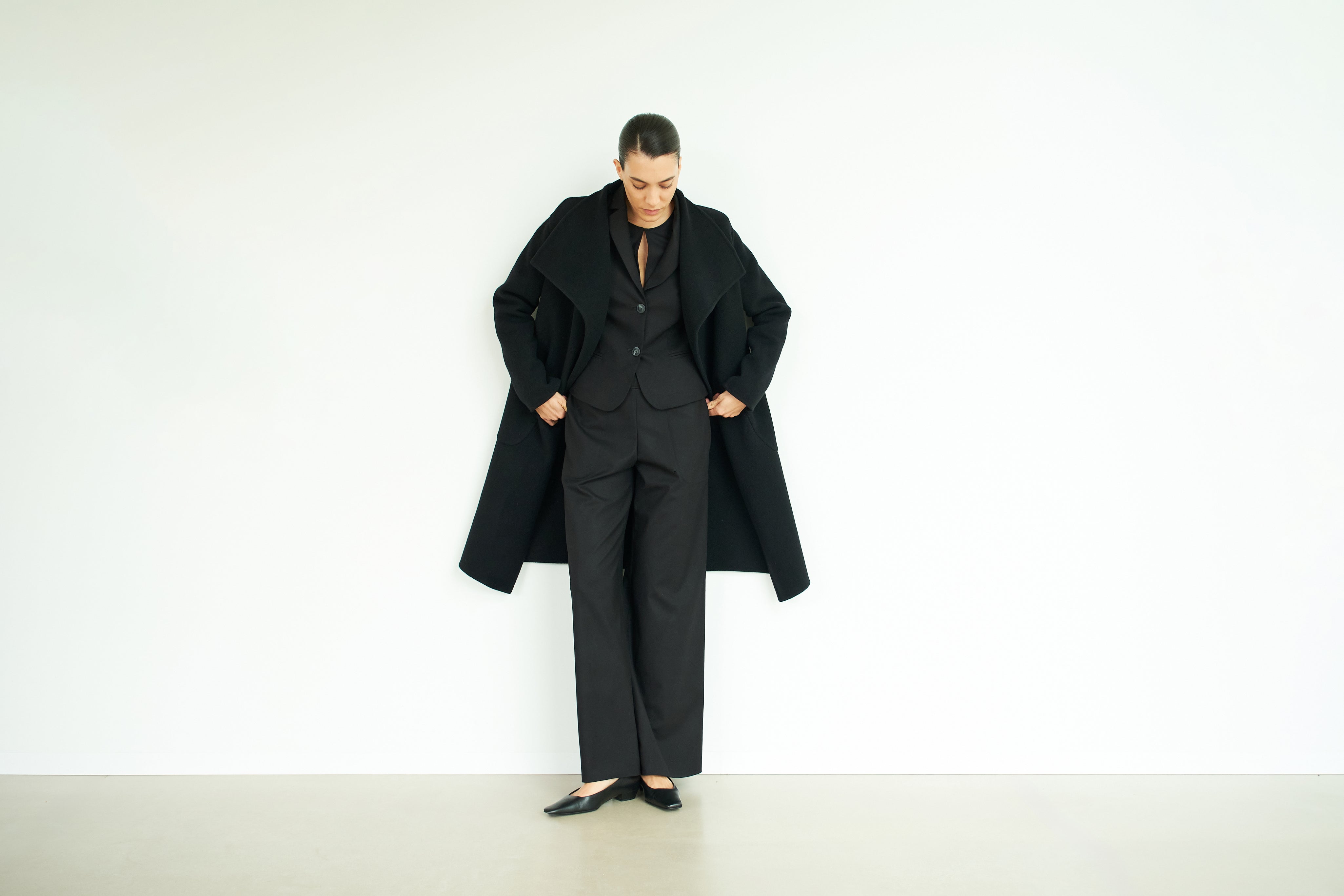 Woman looking down wearing black suit, shoes and coat.