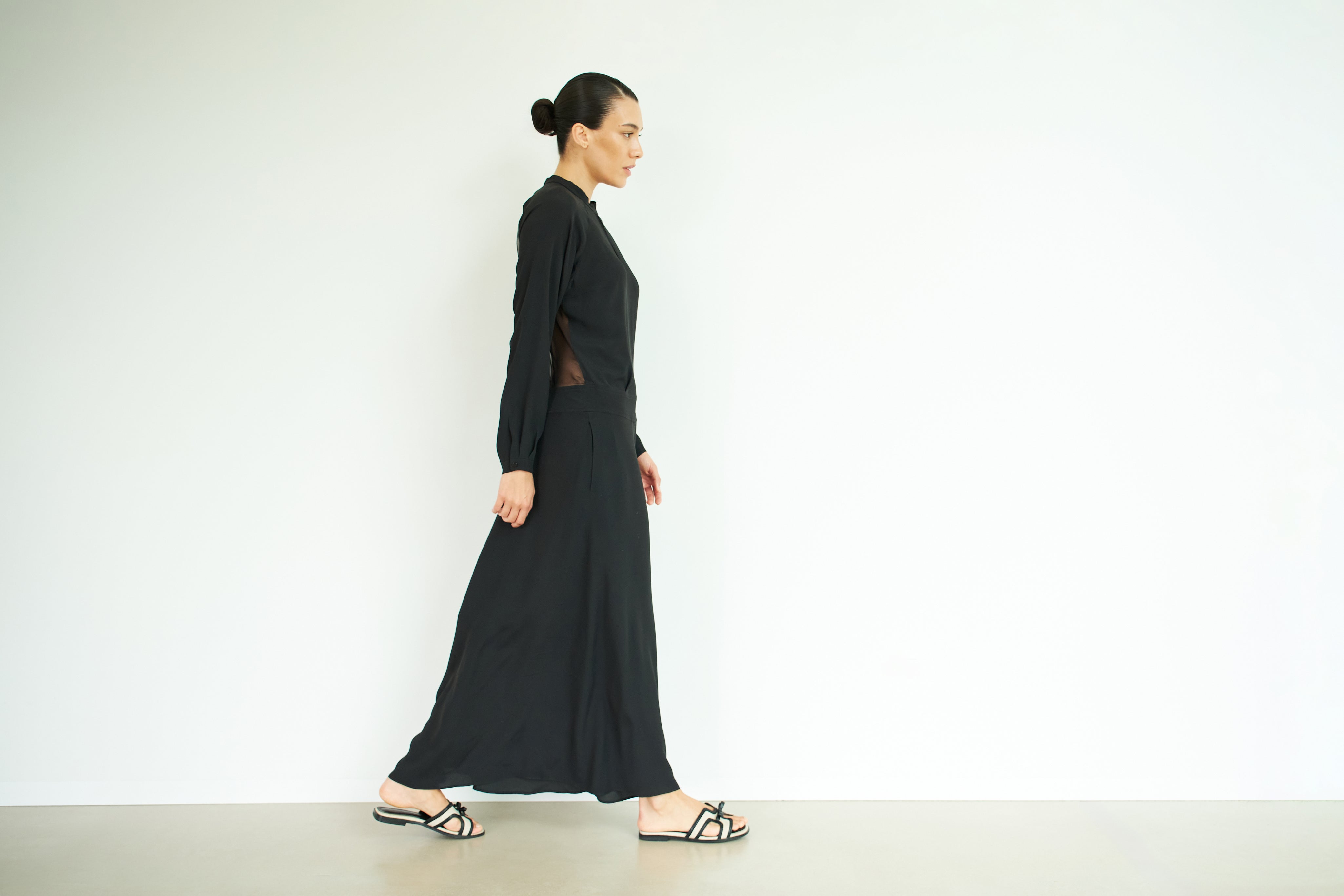 Woman walking to the right in a black full-length dress.