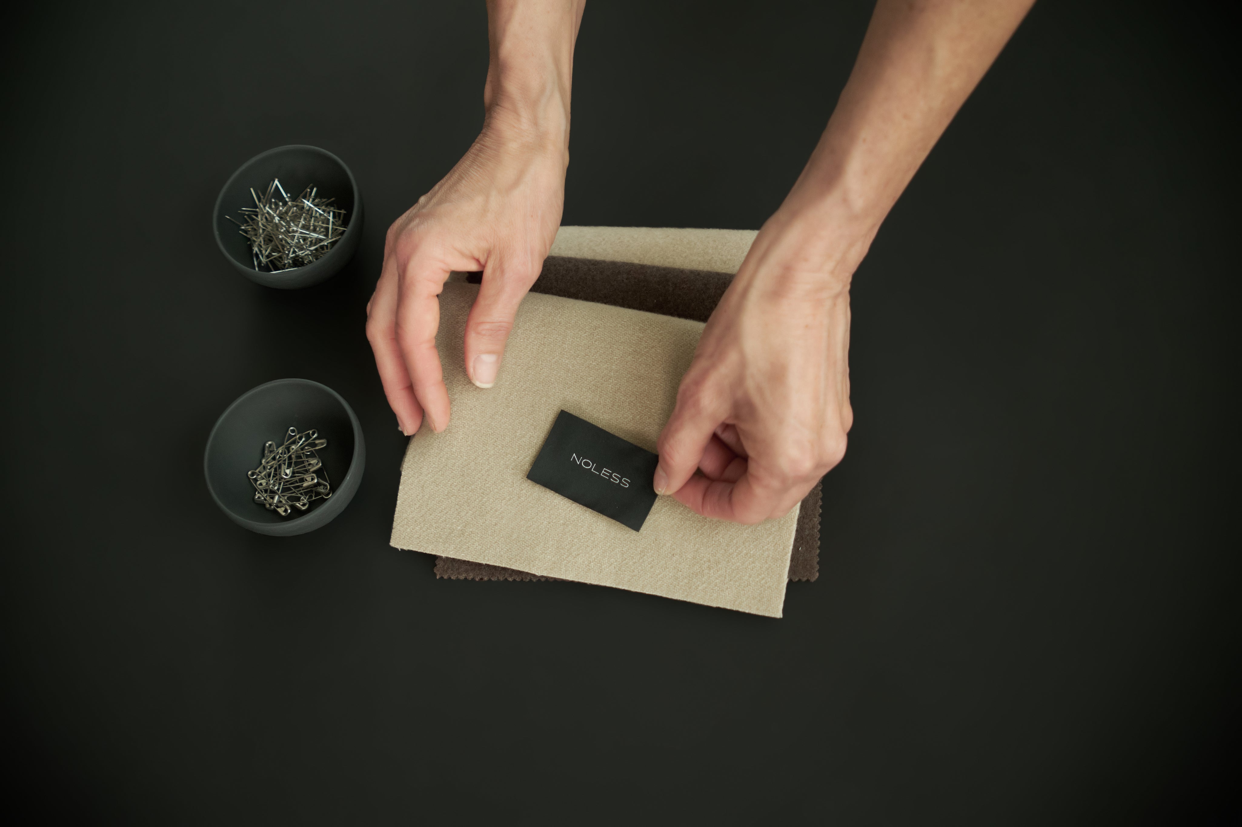 Hands comparing fabric swatches during the NOLESS material-selection process